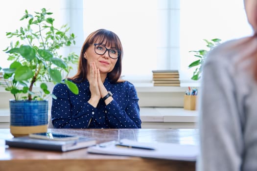Mature sad woman in therapy session with mental professional psychologist, sitting at table in office of therapist counselor social worker. Psychology psychotherapy mental assistance treatment support
