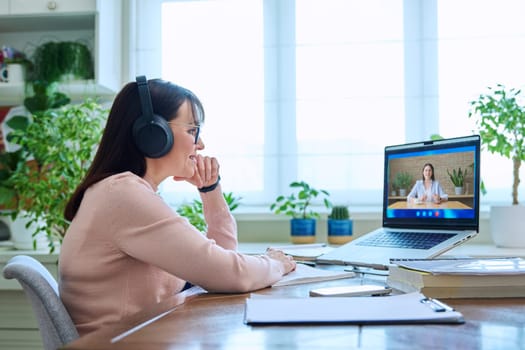 Online work video meeting of two female colleagues. Middle aged woman working remotely in home office talking with client, colleague, student on laptop computer screen. Technology, business, education