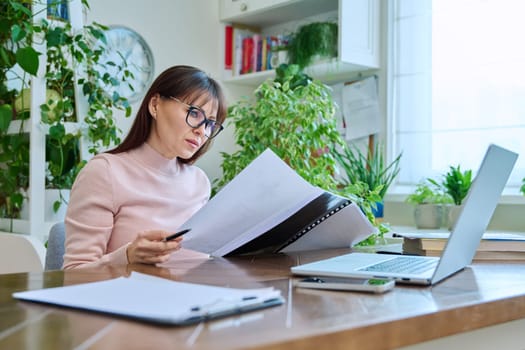 Woman working remotely in home office at workplace with computer. Female professional holding paper contract in hands, architect lawyer accountant preparing documents. Work remotely business freelance