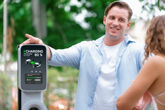 Happy and lovely couple with eco-friendly conscious recharging electric vehicle from EV charging station. EV car technology utilized as alternative transportation for future sustainability. Synchronos