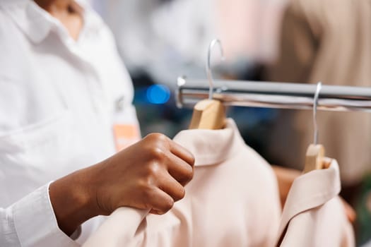 African american woman assistant adjusting jackets on hangers in shopping mall. Clothing store employee hanging trendy blazers from new collection for sale on display rack close up