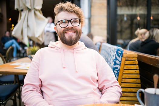 Millennial bearded man having breakfast at table of street cafe on spring day, drinking warm cappuccino. Spring restaurant terrace.