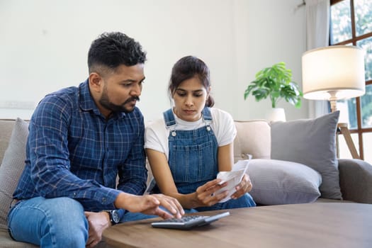 Indian married couple calculating bills, discussing planning budget together, serious wife and husband looking at calculator, checking finances.