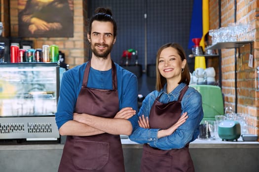 Small business team portrait of confident successful colleagues partners young man woman in aprons posing looking at camera at workplace in restaurant coffee shop cafeteria. Partnership teamwork work