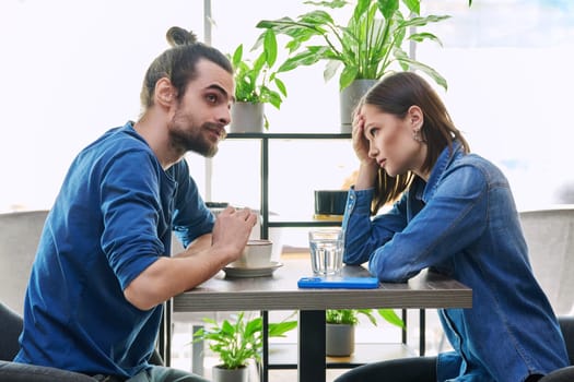 Serious aggressive young couple quarreling, angry, arguing, talking, nervous, sitting together at table in cafeteria. Relationships difficulties problems negative emotions lifestyle people concept