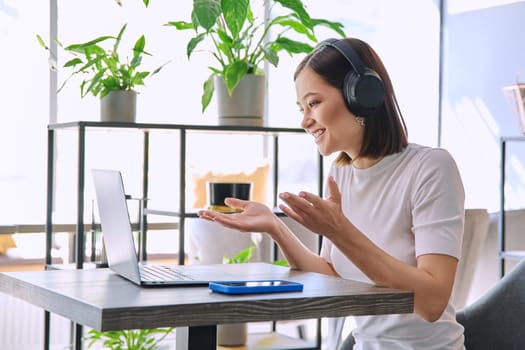 Young woman in headphones having work video chat conference call using laptop computer sitting in cafe workshop. Remote virtual online work study freelance blog vlog, internet technology youth concept