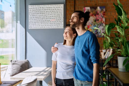 Young happy couple hugging together looking out the window. Love, friendship, romance, relationship, happiness, lifestyle, people concept