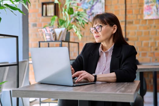 Middle-aged business confident successful serious woman working remotely at table with laptop computer in coworking cafe. Business, mature people, success, leadership, management, empowerment concept