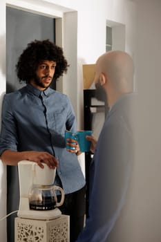 Company employees taking break to chat and drink coffee together in business office. Arab entrepreneur and project manager having casual conversation in corporate coworking space