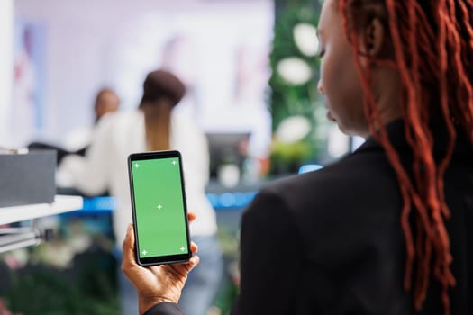 African american woman using smartphone with green screen while shopping for clothes in mall. Boutique buyer holding mobile phone with empty chroma key display for copy space