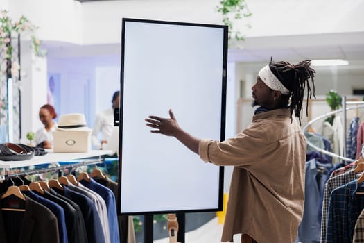 Customer using empty white smart screen to browse clothes in store. African american stylish man touching interactive blank display while shopping for apparel in mall boutique