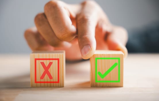 Businessman finger touches between two wooden cubes with check marks depicting right and wrong choices. Communicates validation and decision-making. Think With Yes Or No Choice.