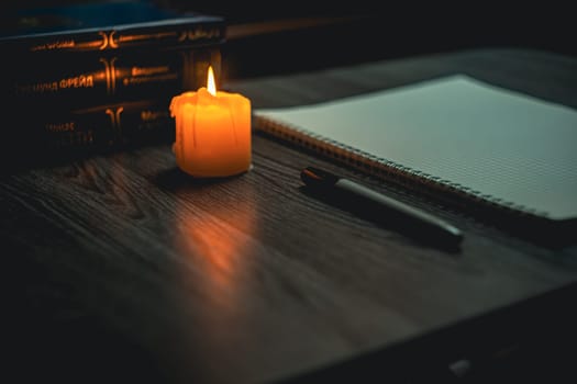 Workplace. A large notepad with a black marker lies on a wooden black table and is illuminated by a candle.. High quality photo