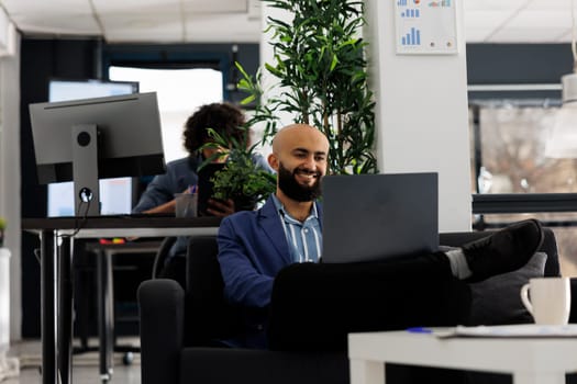 Smiling arabian businessman having videoconference with coworker in a corporate office. Project manager using a laptop for telework meeting in start up company coworking space