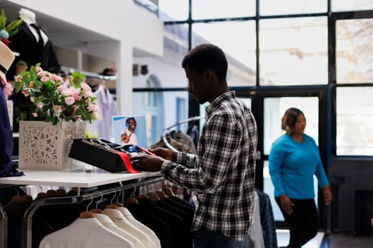 African american customer looking at shelf full with accessories, checking fashionable belt in modern boutique. Stylish man shopping for casual wear in clothing store. Fashion concept