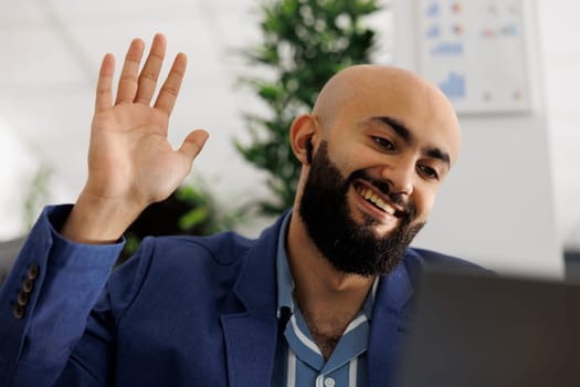 Smiling entrepreneur attending remote conference call and greeting employees. Arab executive manager waving hello to team during virtual videoconference to discuss project
