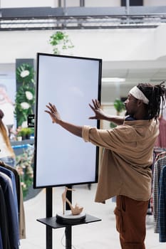 African american man interacting with digital screen offering shoes to customer in shopping center. Clothing store buyer touching white empty display mock up to check stiletto brand options