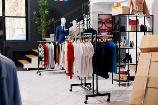 Empty fashion store with casual and formal wear design, retail shop with stylish clothes on hangers and racks. Modern boutique inside of shopping mall, fashionable merchandise on sale.