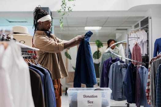 African american man putting casual shirt in donation box while shopping in boutique. Mall customer dropping off second hand apparel in container for charitable organization