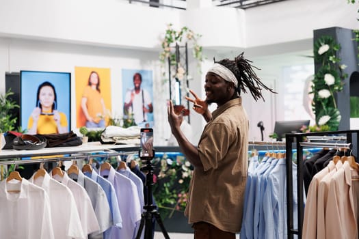 African american influencer promoting latest clothing collection in store. Man blogger recording video with apparel brand advertising to share through social media accounts
