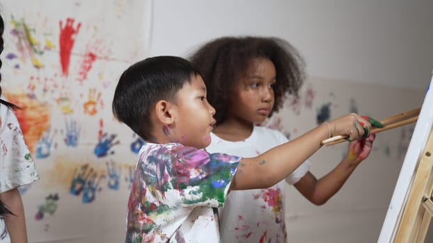 Happy creative african girl painted or draw canvas together with asian boy. Group of playful student create funny painting or artwork painted by watercolor. Creativity activity concept. Erudition.