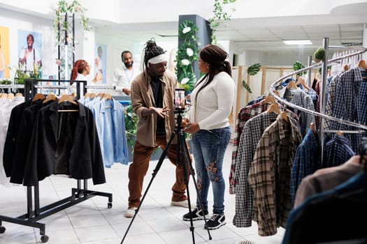 African american influencers advertising fashion brand, showing clothes on smartphone camera. Blogger discussing trends and asking customer for opinion while promoting boutique
