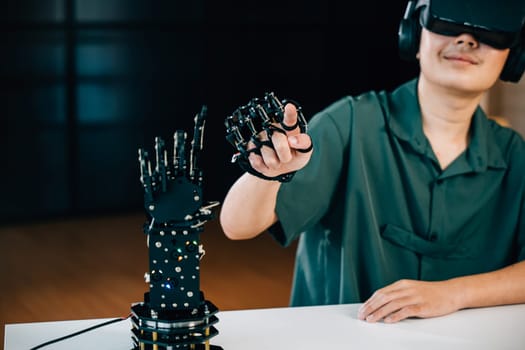 In a classroom an Asian teenager uses VR glasses for a robot arm project. Blending robotics programming with STEM education exploring futuristic technology. moves a robotic hand