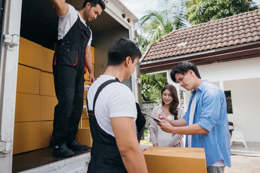 Newlywed couple signs the delivery checklist with professional moving team after furniture handling. Employees in uniform show teamwork ensuring customer satisfaction. Moving Day Concept