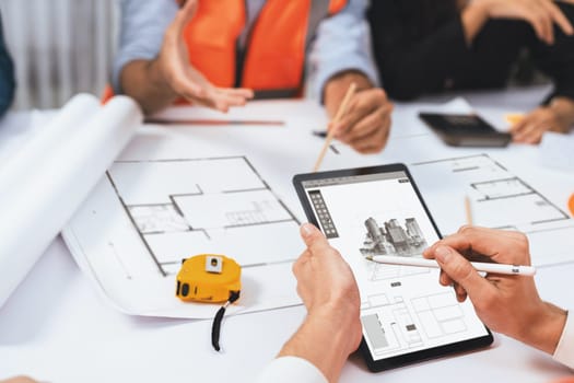 Diverse group of civil engineer and client working together on architectural project, reviewing construction plan and building blueprint using tablet at meeting table. Prudent