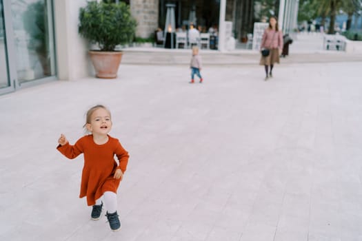 Little girl runs along a wide street, holding her hem. High quality photo