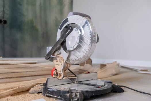 The miter saw or a multi material construction saw on the floor of the apartment with tape measure and wood. Renovation of the house