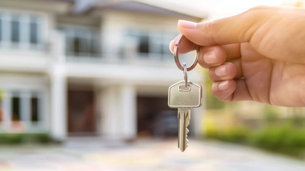 A person is holding a key in front of a house.