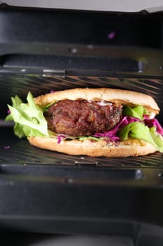 Sandwich with meatballs, lettuce, and red cabbage grilling.