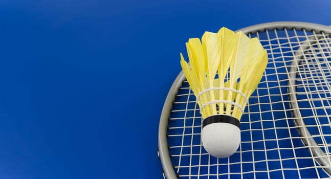 Yellow badminton feather shuttlecock on badminton racket over a blue background, banner size image with copy space