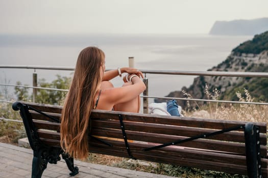 Woman travel sea. Happy tourist taking picture outdoors for memories. Woman traveler looks at the edge of the cliff on the sea bay of mountains, sharing travel adventure journey.