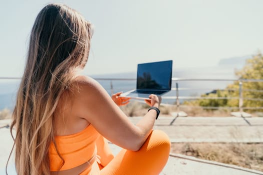 Digital nomad, Business woman working on laptop by the sea. Pretty lady typing on computer by the sea at sunset, makes a business transaction online from a distance. Freelance, remote work on vacation