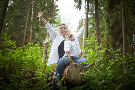 Funny mother with dreadlocks and fat boy happy hugging in forest on a sunny summer day