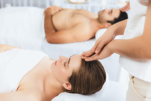 Caucasian couple enjoying relaxing anti-stress head massage and pampering facial beauty skin recreation leisure in dayspa modern light ambient at luxury resort or hotel spa salon. Quiescent