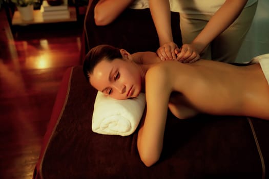 Caucasian couple customer enjoying relaxing anti-stress spa massage and pampering with beauty skin recreation leisure in warm candle lighting ambient salon spa at luxury resort or hotel. Quiescent