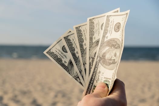 Unrecognizable woman Displaying Spread of Cash dollars bills on sandy beach coastline. Concept finance saving money for holiday vacation. Costs in travel holidays. Extra money, passive income