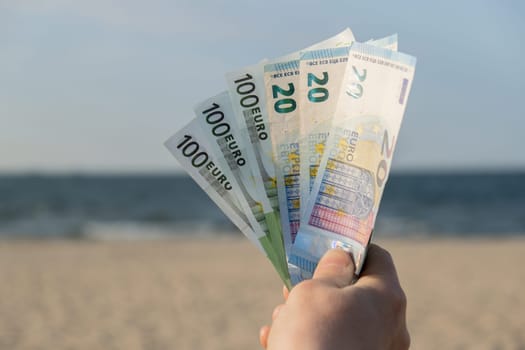 Unrecognizable woman Displaying Spread of Cash euros bills on sandy beach coastline. Concept finance saving money for holiday vacation. Costs in travel holidays. Extra money, passive income