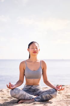 young asian woman doing meditation at beach sitting with legs crossed, concept of mental relaxation and healthy lifestyle, copy space for text