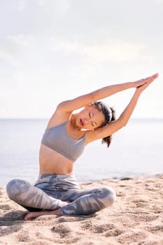 young asian woman doing yoga exercises at beach sitting with legs crossed, concept of mental relaxation and healthy lifestyle, copy space for text