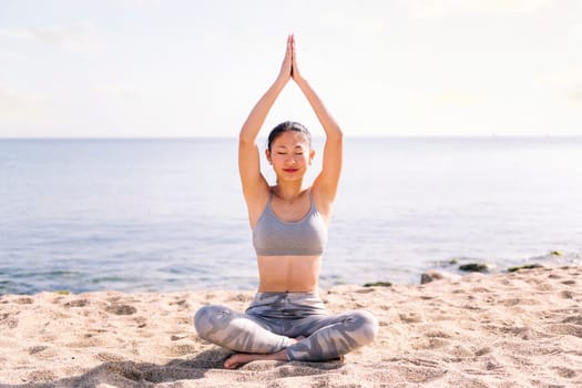 young asian woman doing yoga exercises at beach sitting with legs crossed, concept of mental relaxation and healthy lifestyle, copy space for text