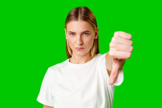 Young Woman Expressing Disapproval With a Thumbs Down Gesture Against a Green Background in studio