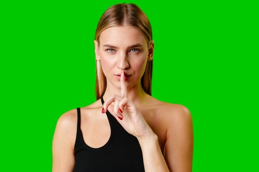 Young Woman Gesturing Silence With Finger on Lips Against Green Screen Background in studio