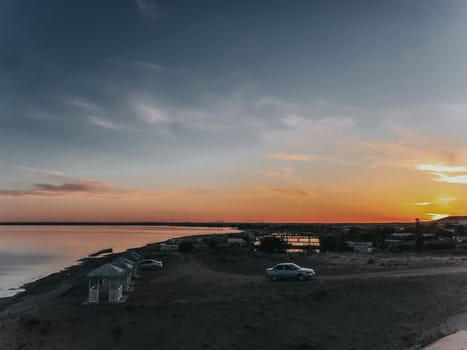 A car parked on a hill, sunset colors the sky, city lights twinkle. Scenic view, travel vibes, wanderlust adventure.