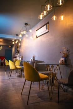 Cozy restaurant interior with glass tables, yellow chairs, textured walls, and pendant lights hanging from the ceiling.