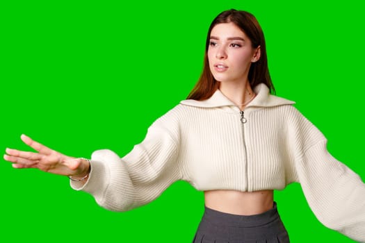 A smiling young woman wearing a casual white hoodie stands against a vibrant green screen background. She is gesturing upwards with her index finger, as if pointing out something important or having a bright idea.