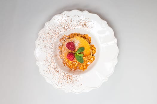 Fluffy pancakes with raspberries and mint leaves on a white plate against a clean white background. Close-up shot.